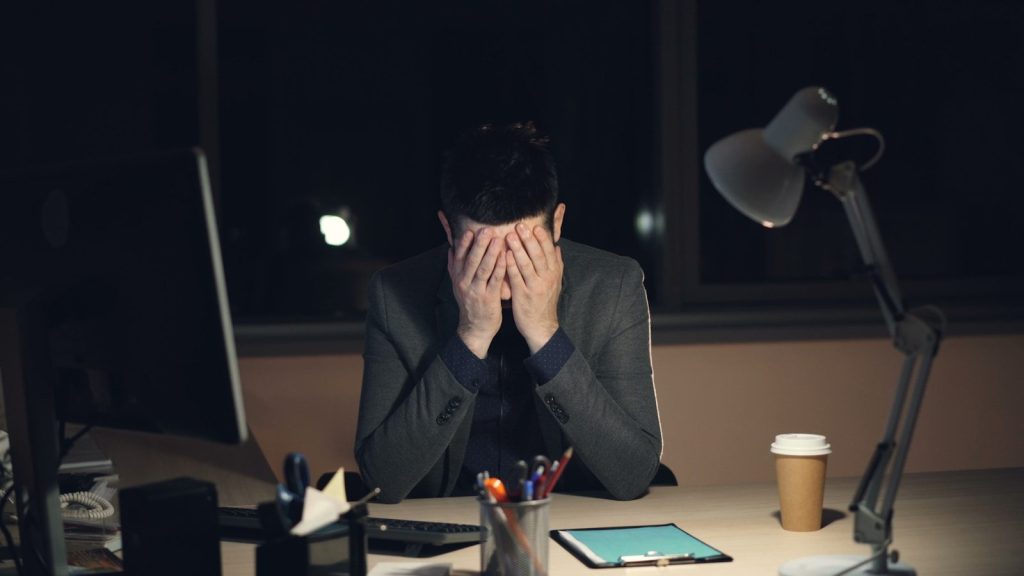 Man in suit sits at desk, head in hands.